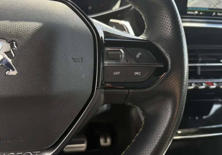 Gros plan sur le volant cuir perforé noir du Peugeot 2008 GT 2021, avec commandes multimédia et surpiqûres vertes visibles.