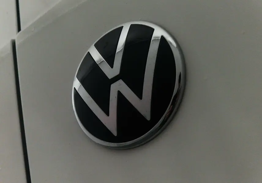 Gros plan sur le logo Volkswagen noir et chrome sur la carrosserie blanche du Caddy Maxi 4 Motion 2025.