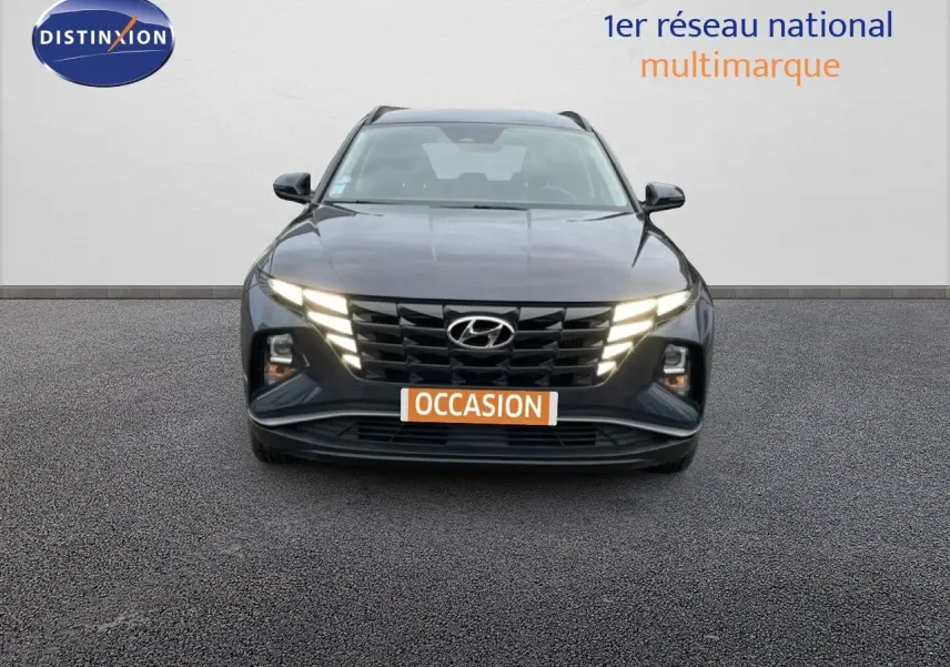 Vue frontale d'un Hyundai Tucson 2023 hybride en Dark Knight Metal avec feux LED allumés sur fond neutre.
