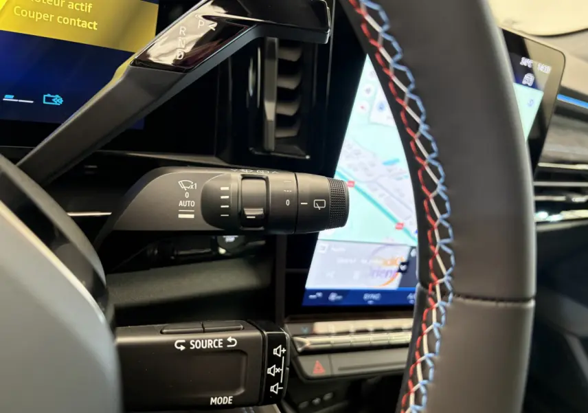 Gros plan intérieur sur le volant noir avec surpiqûres tricolores et la commande de clignotants du Renault Espace blanc 2025.