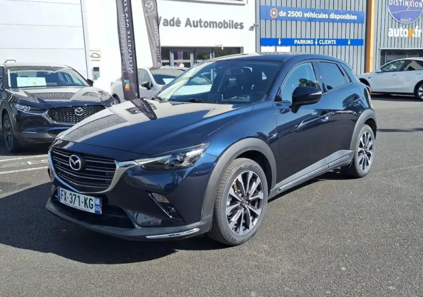 Mazda CX-3 bleu en 3/4 avant droit, avec jantes aluminium et calandre chromée visible en extérieur.