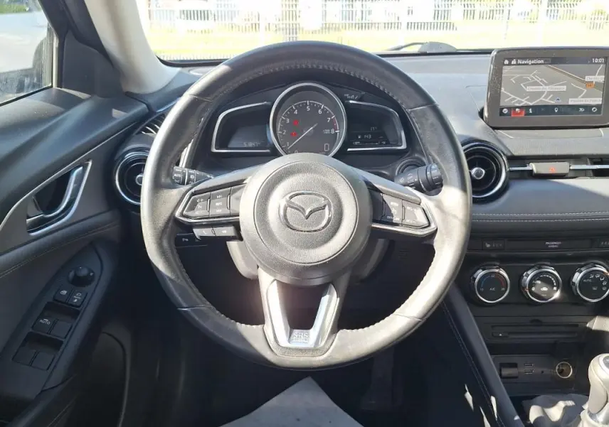Vue intérieure centrée sur le volant cuir multifonctions d'une Mazda CX-3 2021 avec écran tactile GPS visible.