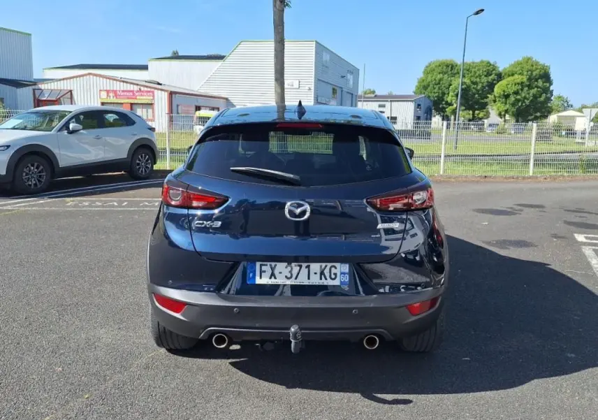 Vue arrière d'un Mazda CX-3 bleu avec attelage et double sortie d'échappement, stationné en extérieur.