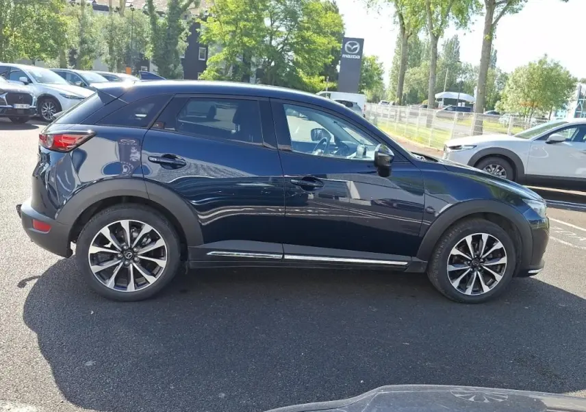 Vue de profil côté gauche d'un Mazda CX-3 bleu 2021 avec jantes alliage et vitres surteintées.