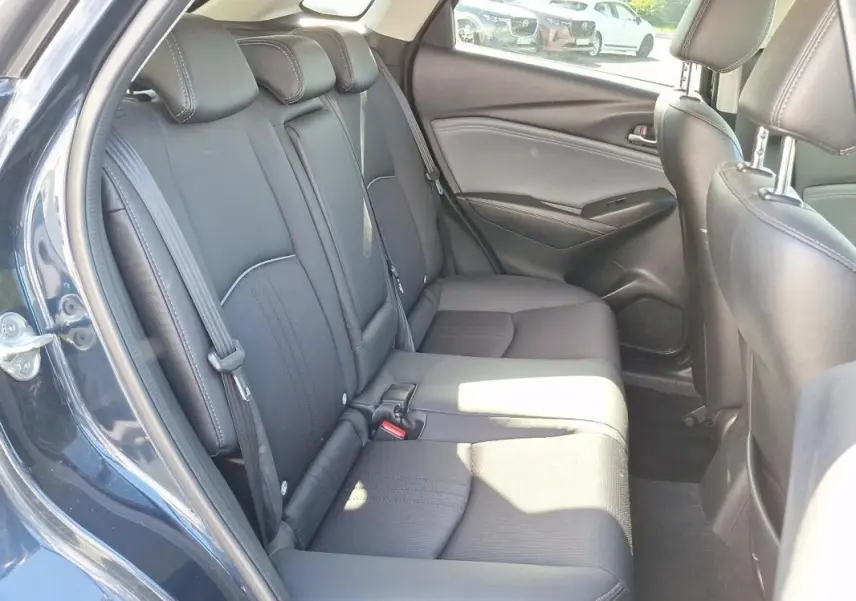 Vue intérieure côté gauche des sièges arrière noirs d'un Mazda CX-3 bleu, avec ceintures de sécurité visibles.