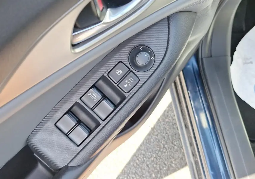 Gros plan sur la commande des vitres et rétroviseurs côté conducteur d’une Mazda CX-3 bleu 2021.