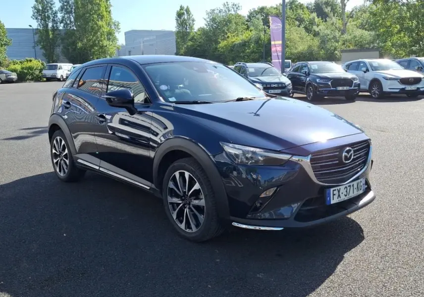 Mazda CX-3 bleu foncé vue 3/4 avant droit, jantes alliage et calandre chromée visible en extérieur.