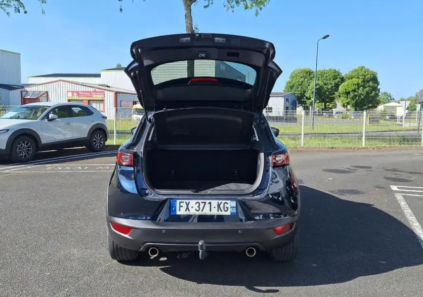 Vue arrière d'un Mazda CX-3 bleu 2021 avec coffre ouvert et attelage visible en stationnement.