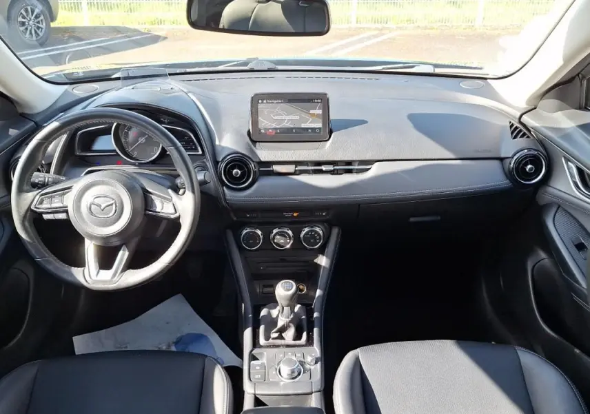 Vue intérieure frontale du tableau de bord noir du Mazda CX-3 2021 avec volant cuir multifonctions et écran tactile GPS.