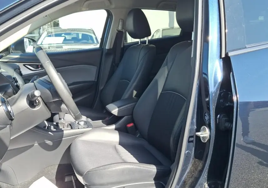 Vue intérieure côté conducteur du Mazda CX-3 bleu 2021, sièges en cuir noir et volant multifonctions visible.