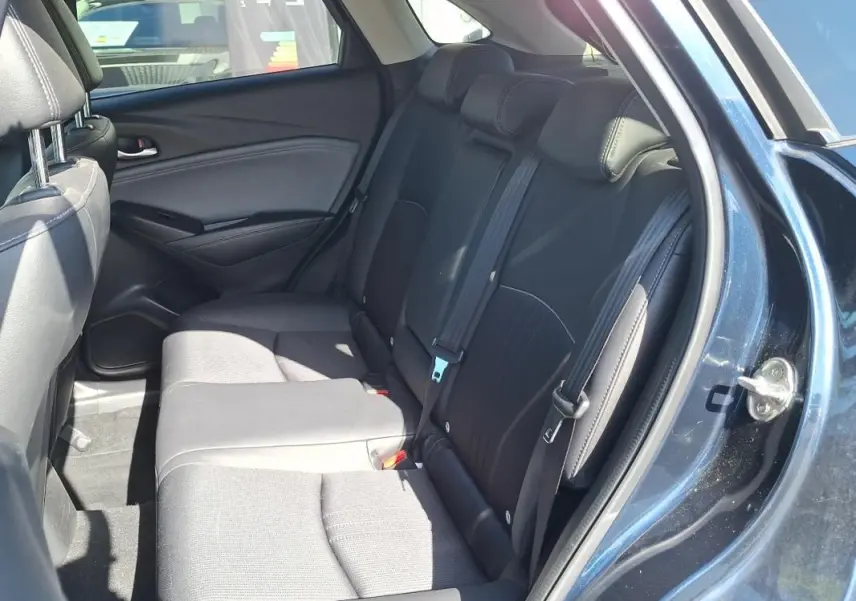 Vue intérieure côté droit des sièges arrière noirs du Mazda CX-3 bleu 2021 avec ceintures de sécurité visibles.