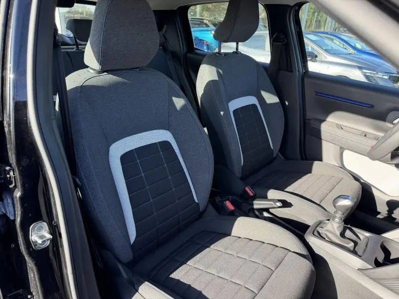 Vue intérieure côté conducteur de la Citroën C3 1.2 Turbo 100ch PLUS 2025 noire avec sièges tissu gris à motifs carrés.