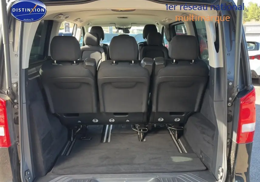Vue arrière du coffre ouvert d’un Mercedes Classe V 220 d long noir, montrant les sièges arrière en tissu noir.