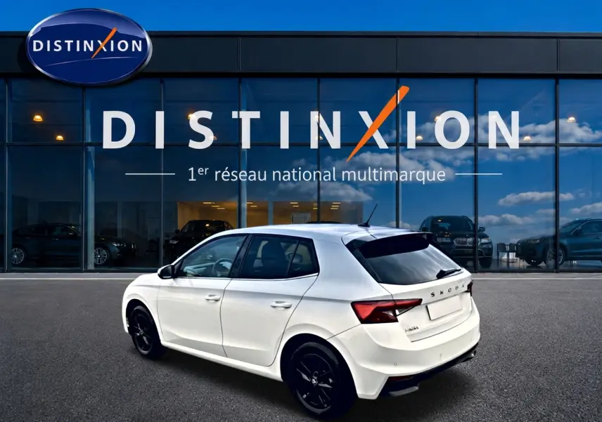 Vue 3/4 arrière droite d'une Skoda Fabia blanche 2025 avec jantes noires, garée devant une vitrine Distinxion.