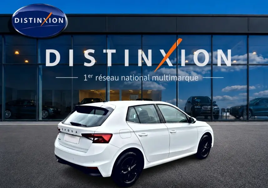 Vue 3/4 arrière droite d'une Skoda Fabia blanche 2025 avec jantes noires, stationnée devant une vitrine Distinxion.