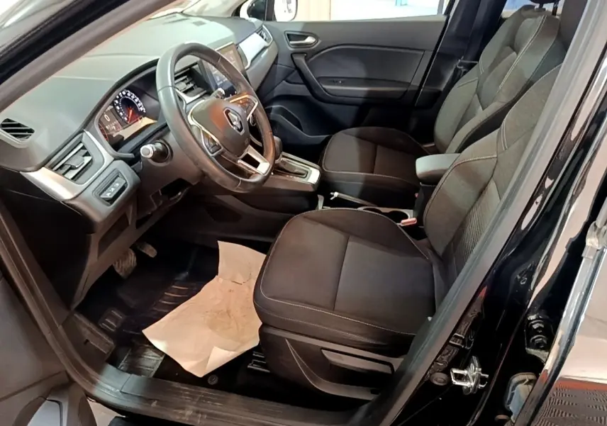 Vue intérieure côté conducteur du Renault Captur noir 2021, volant multifonctions et sièges tissu noirs visibles.