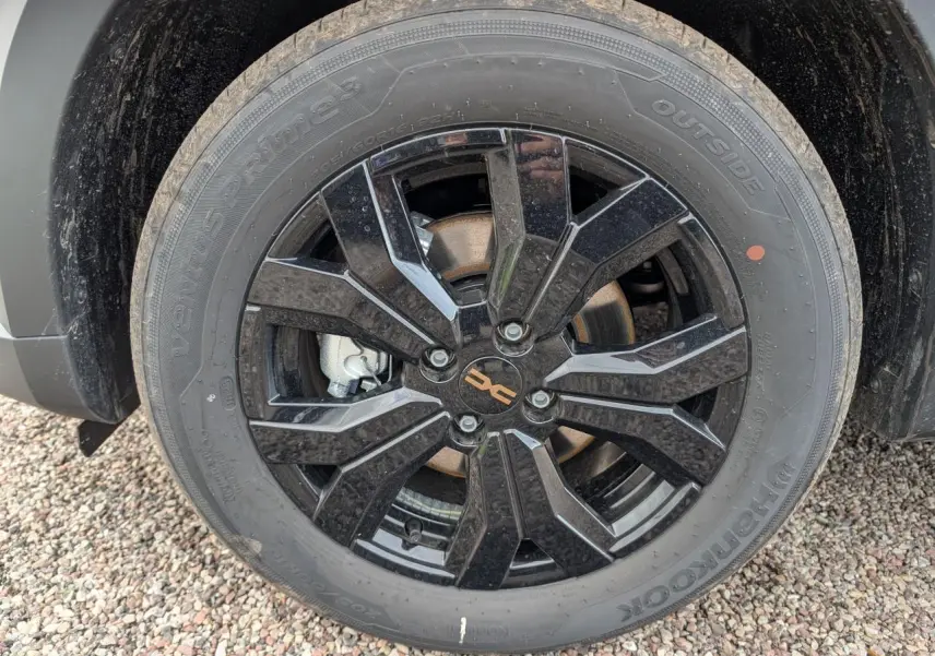 Gros plan sur la jante noire brillante 16 pouces du Dacia Jogger gris métallisé, avec logo Dacia brun cuivré au centre.