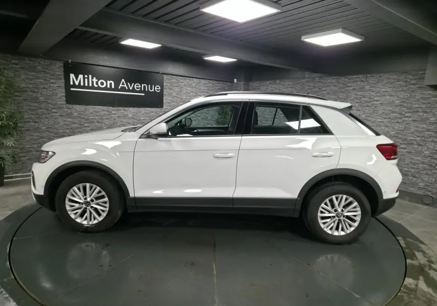 Vue de profil côté gauche d'un Volkswagen T-Roc blanc avec jantes alliage et toit ouvrant en showroom.