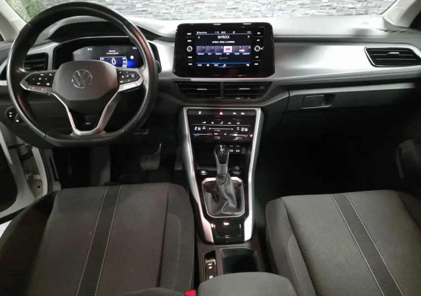 Vue intérieure avant du Volkswagen T-Roc blanc 2022, tableau de bord gris métallisé avec écran tactile et volant cuir multifonction.