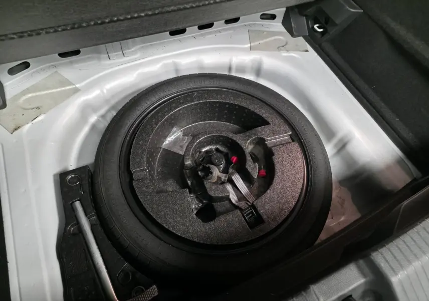 Vue plongeante sur la roue de secours et le coffre blanc du Volkswagen T-Roc 2.0 TDI 2022, avec outils de changement visibles.