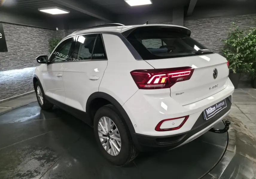 Vue 3/4 arrière droite du Volkswagen T-Roc blanc avec attelage amovible et feux arrière LED allumés en intérieur showroom.