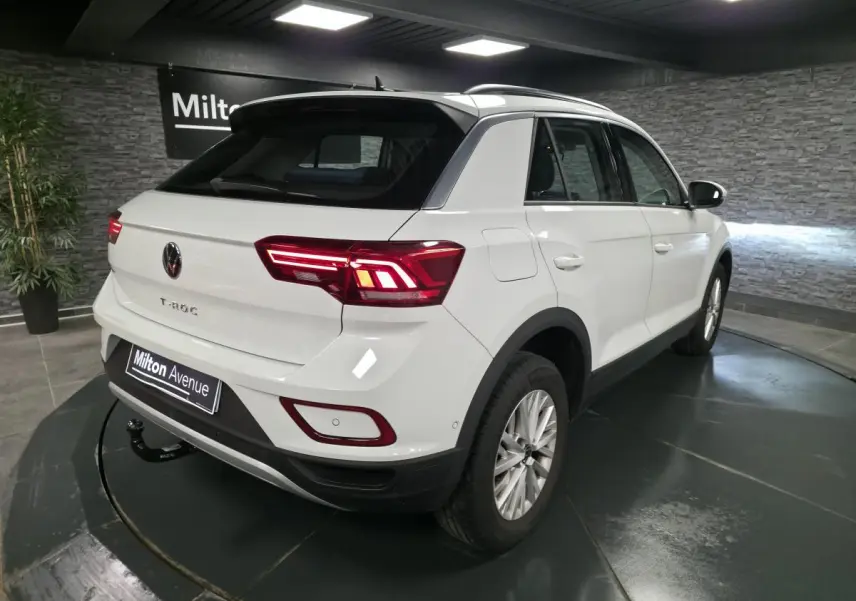 Volkswagen T-Roc blanc en 3/4 arrière droit, avec attelage amovible et feux arrière LED allumés.
