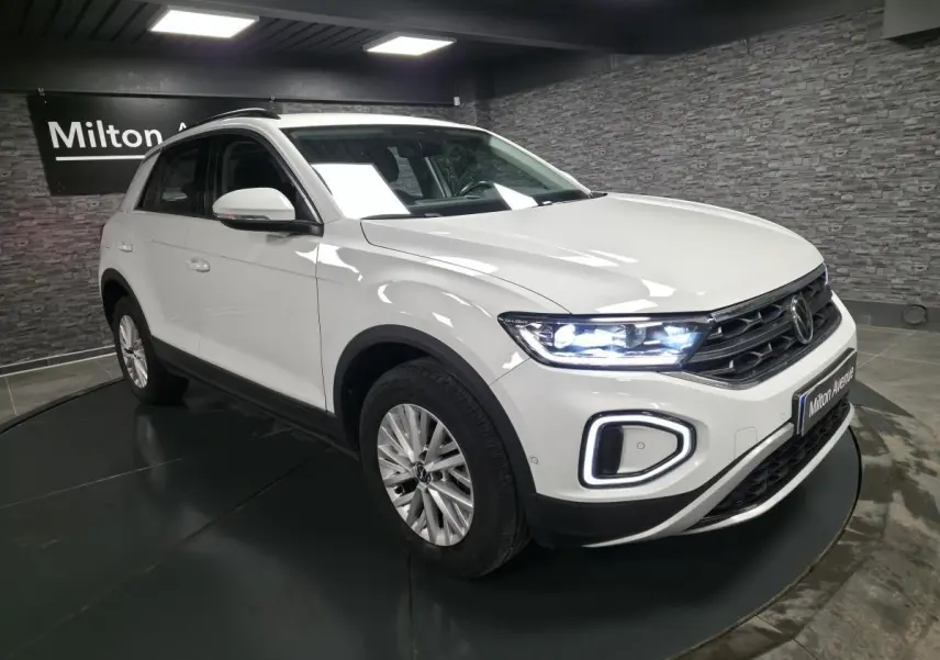 Volkswagen T-Roc blanc vue 3/4 avant droit avec phares LED allumés en intérieur showroom.