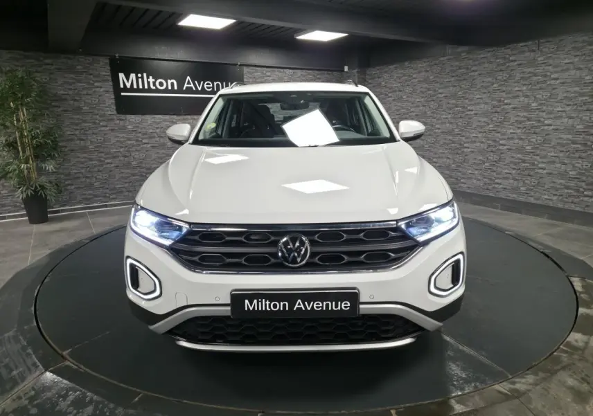 Vue avant d'un Volkswagen T-Roc blanc avec feux LED allumés dans un showroom intérieur.