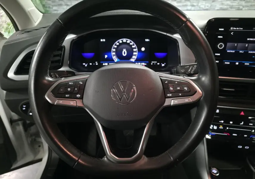 Vue rapprochée du volant en cuir noir multifonction du Volkswagen T-Roc blanc avec tableau de bord digital allumé.