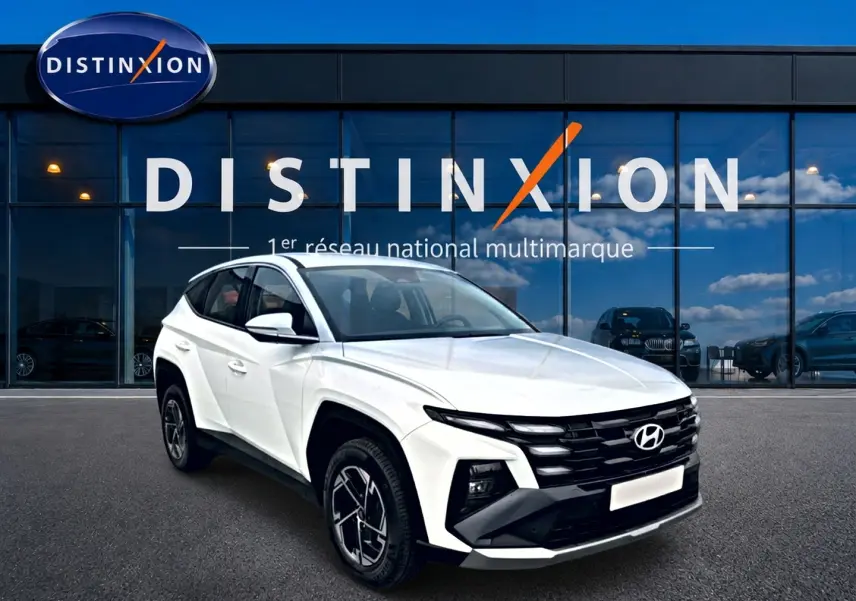 Vue 3/4 avant droit du Hyundai Tucson blanc 2026 avec calandre noire et jantes alliage 17 pouces devant un showroom Distinxion.