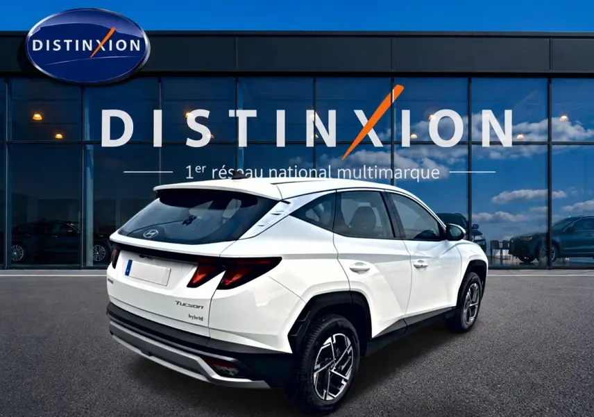 Vue 3/4 arrière droite du Hyundai Tucson blanc hybride devant une vitrine avec logo Distinxion.