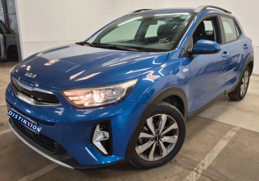 KIA Stonic bleu 2024 en 3/4 avant droit, avec phares allumés et jantes alliage distinctives.