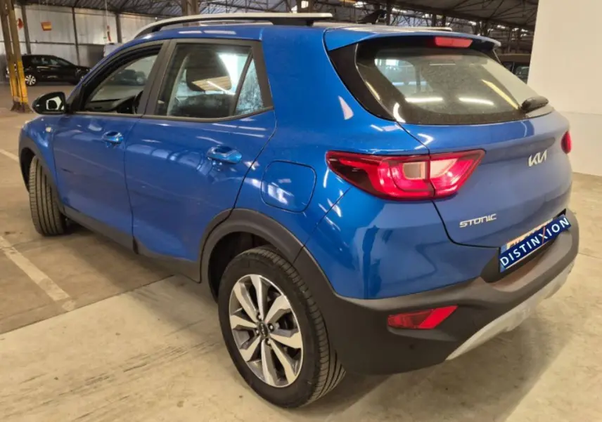 Vue 3/4 arrière droite du KIA Stonic bleu 2024 avec feux arrière allumés et jantes alliage distinctives.