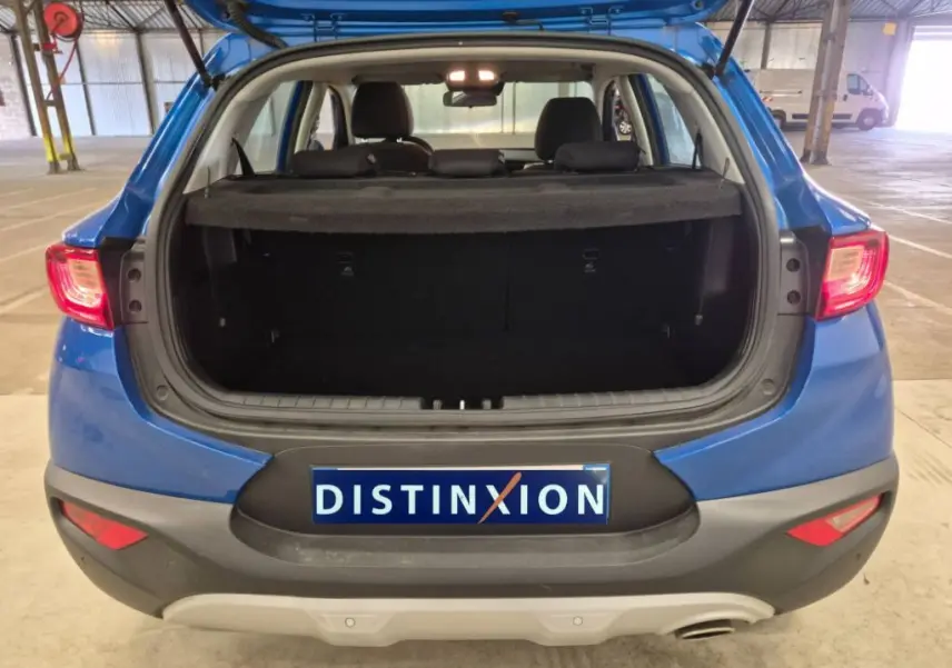 Vue arrière d’un KIA STONIC bleu 2024 avec coffre ouvert, mettant en valeur l’espace de chargement et les feux arrière allumés.