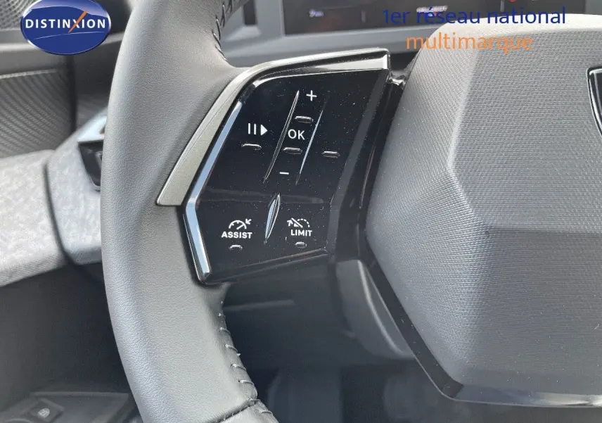 Gros plan sur les commandes gauche du volant en cuir noir du Peugeot 3008 Hybrid bleu Ingaro Metal, tableau de bord en arrière-plan.