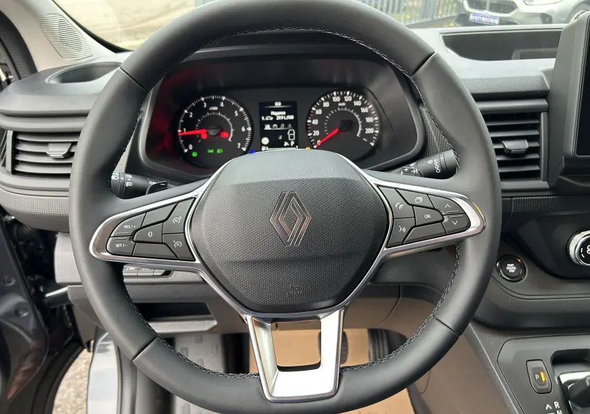 Vue rapprochée du volant cuir noir avec commandes multifonctions du Renault Trafic Fourgon gris Comète 2025.