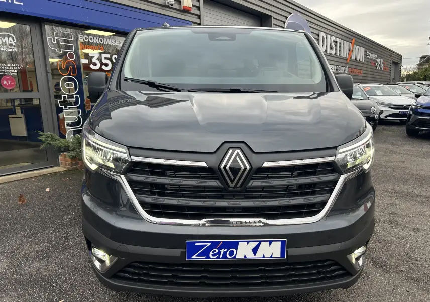 Vue frontale d’un Renault Trafic Fourgon Advance gris Comète avec phares allumés et plaque Zéro KM.