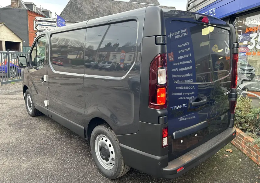 Renault Trafic Fourgon gris Comète vu en 3/4 arrière droit, avec feux arrière allumés et porte latérale coulissante.
