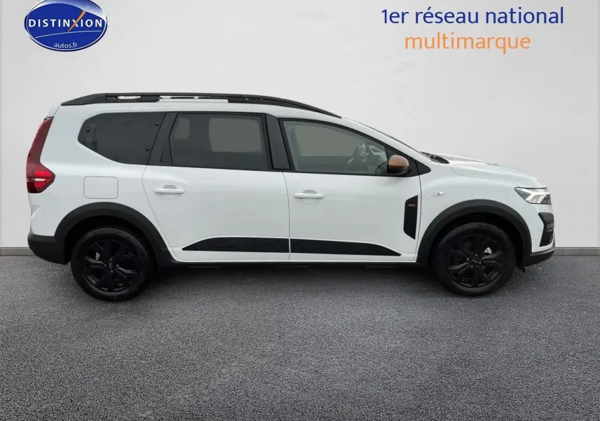 Profil droit d’un Dacia Jogger blanc 2025 avec barres de toit noires et jantes alliage sombres.