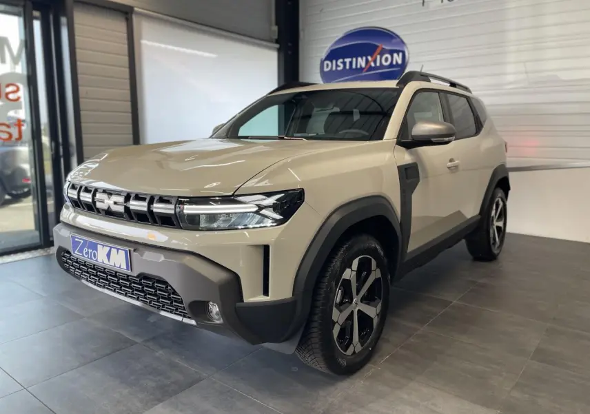 Vue 3/4 avant d'un Dacia Duster beige Sandstone 2025 avec jantes alliage 18 pouces et barres de toit noires.