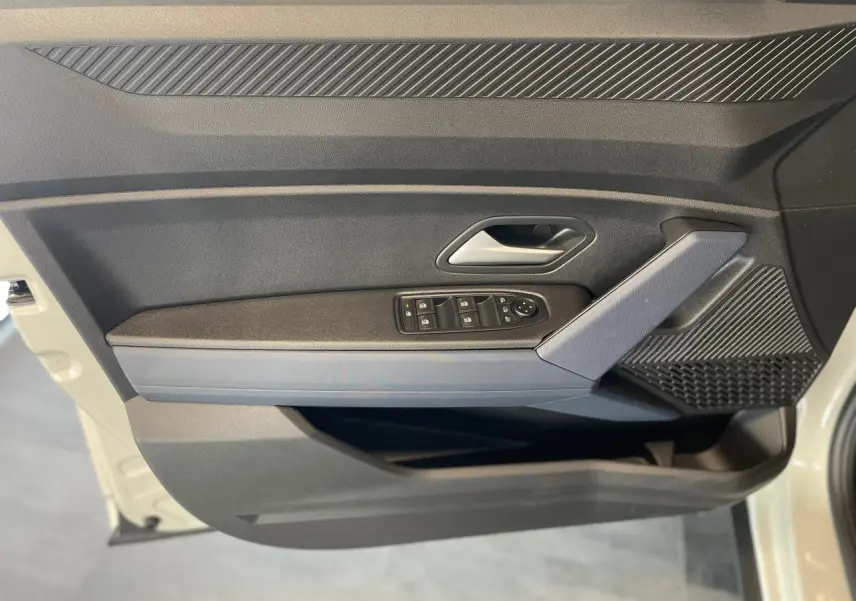 Vue latérale du panneau de porte avant gauche beige du Dacia Duster 2025 avec commandes de vitres et accoudoir Denim Bleu.
