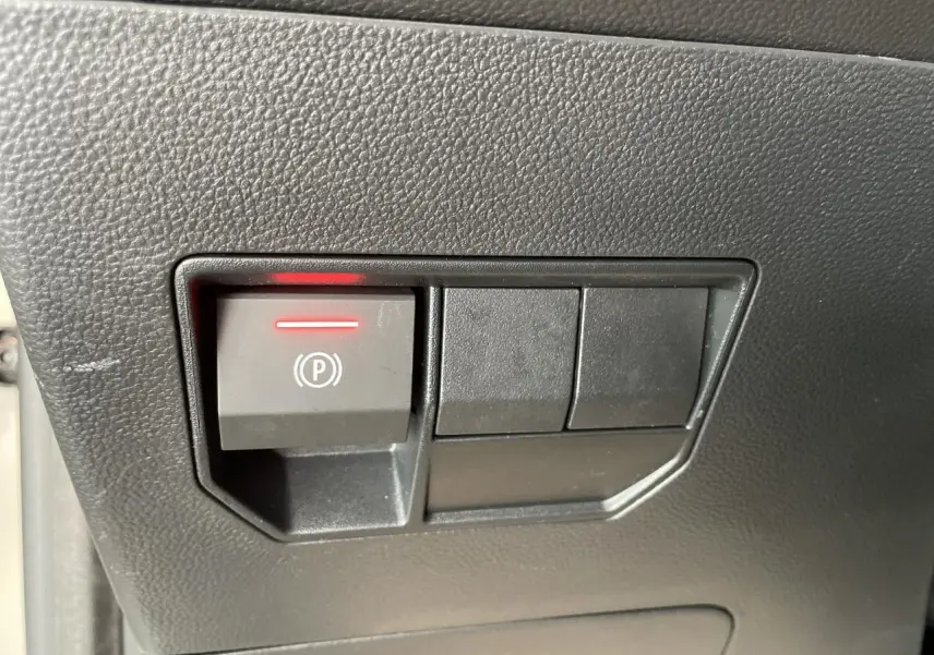 Gros plan sur le bouton de frein de stationnement électrique avec témoin rouge sur la console intérieure noire du Dacia Duster beige.