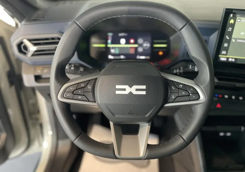 Vue rapprochée du volant noir du Dacia Duster 2025 avec commandes intégrées et tableau de bord digital en arrière-plan.