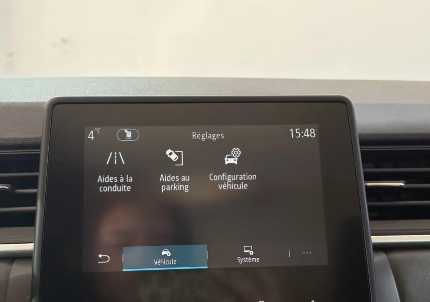 Gros plan sur l'écran tactile central du Renault Captur bleu 2024 affichant les réglages d'aides à la conduite et au parking.