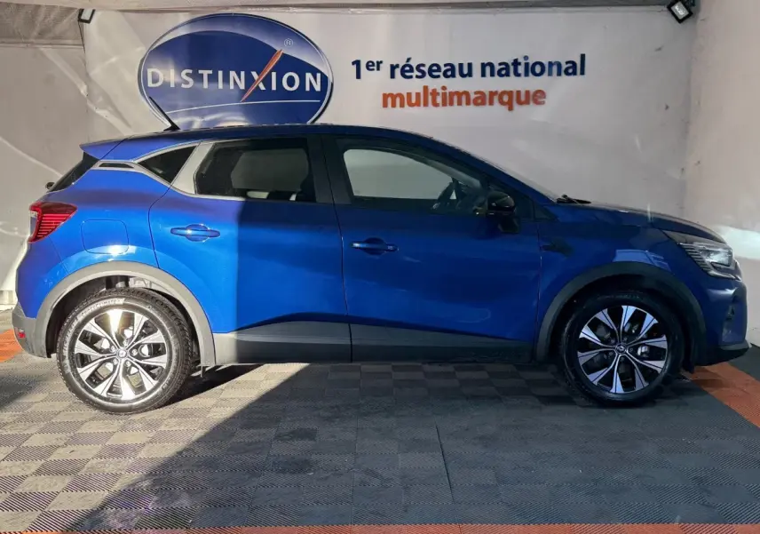 Profil droit d'un Renault Captur bleu 2024 avec jantes alliage et toit noir dans un showroom intérieur.