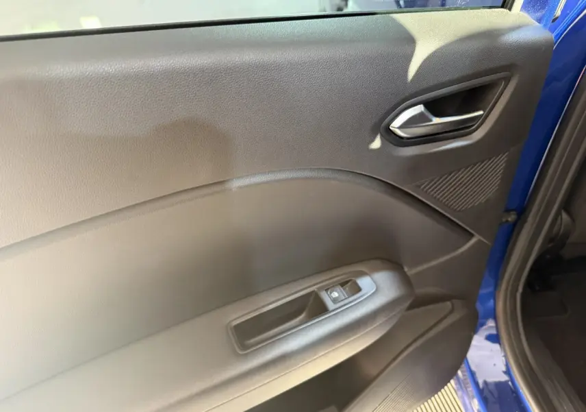 Détail de la porte avant gauche intérieure noire du Renault Captur bleu 2024, avec poignée argentée et commande de vitre.