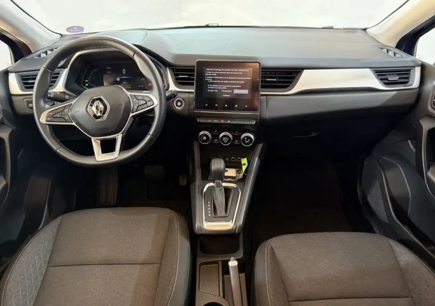 Vue intérieure avant du Renault Captur bleu 2024, volant multifonctions cuir synthétique et écran tactile central vertical.