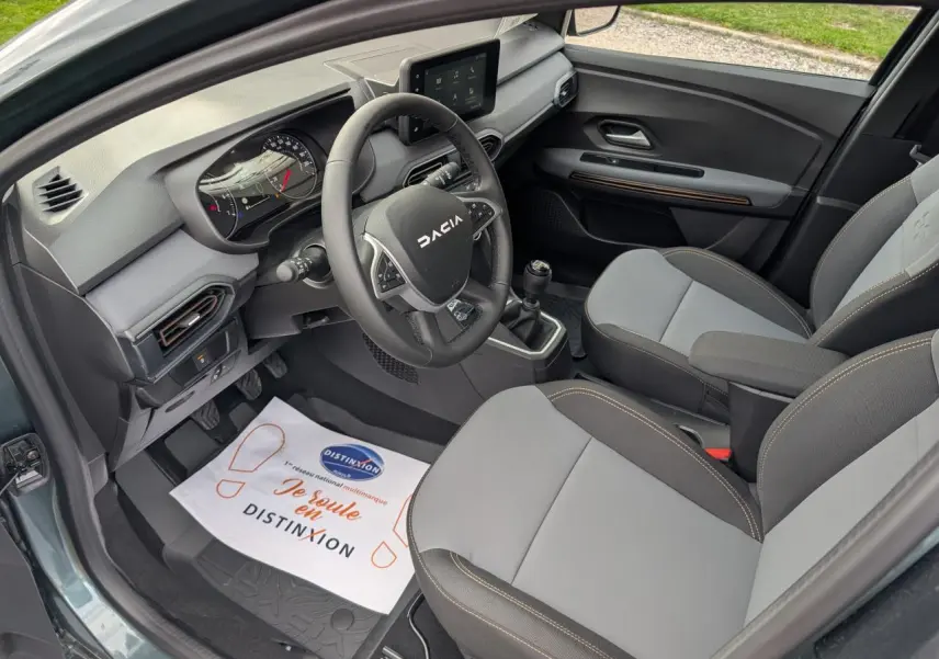 Vue intérieure côté conducteur du Dacia Jogger 2025 vert métallisé, avec volant, tableau de bord et sièges gris à surpiqûres brun cuivré.