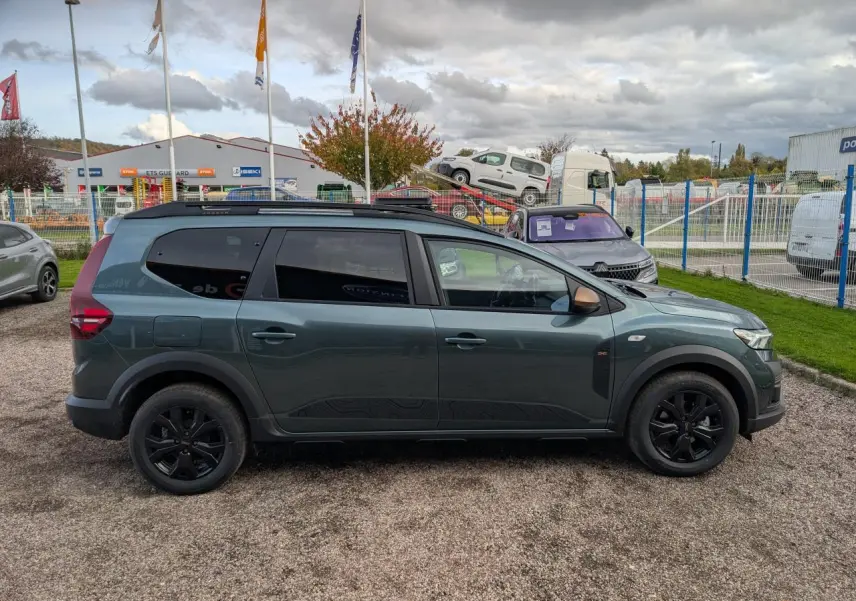 Vue de profil côté gauche d’un Dacia Jogger vert métallisé avec jantes noires et barres de toit noires.