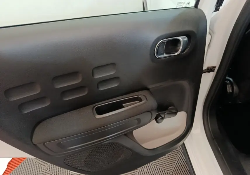 Vue intérieure de la porte arrière droite blanche d'une Citroën C3 2020 avec poignée chromée et manivelle de vitre.